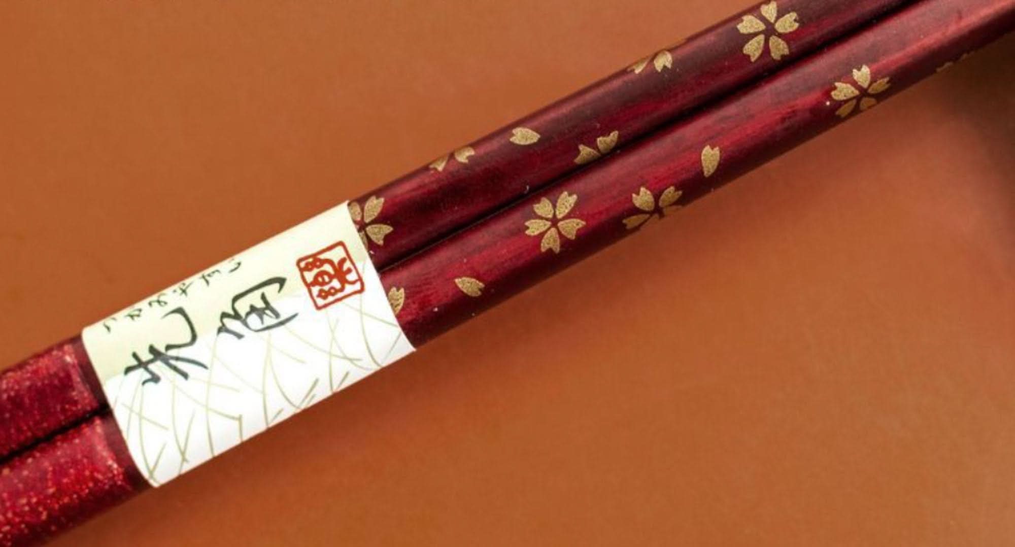 Japan Imported Sunlife Handmade Solid Wood Chopsticks, dark red with gold cherry blossoms, on a warm brown surface.